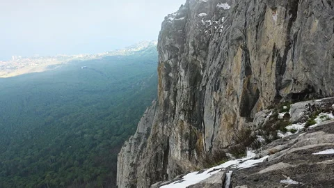 Steep Rocky Wall Descending Into Trees. Distant City Skyline Blurred Behind Видео 335267906