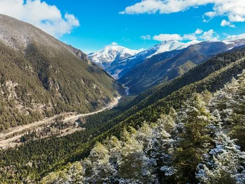 Steep valley slopes covered in trees with road and snowy mountains Photos
