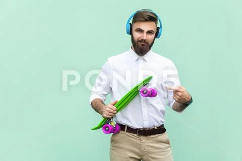 Steep young man with blue headset and holding arms penny skateboard. Light gr Stock Photos