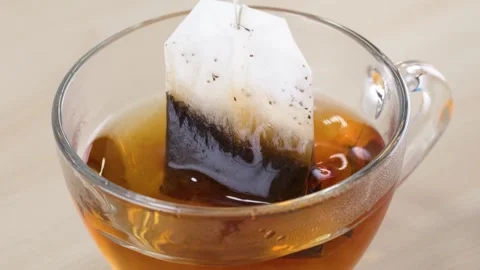 Steeping Black Tea Bag in Clear Glass Cup on Wooden Table Stock Footage 345767615