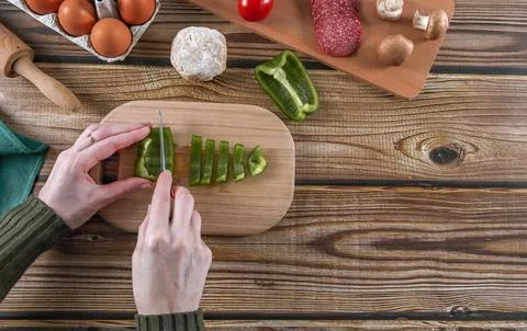 Step 10: Womans hands cutting peppers for pizza dough on a wooden table. Stock Photos