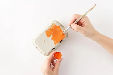 Step in creative process. Painting an egg carton orange with a brush for a .. 스톡 사진