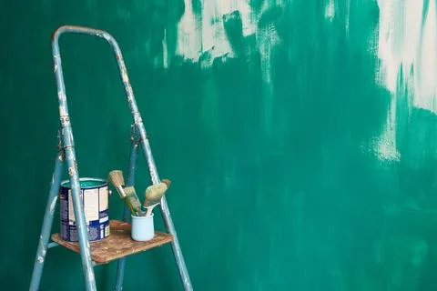 Stepladder, brushes and paint on the background of a green unpainted wall. Stock Photos