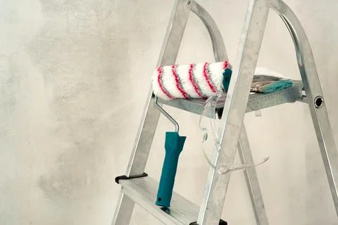 Stepladder, paint roller, brush on the background of a concrete wal Foto stock