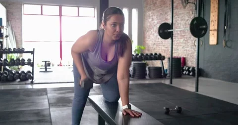Stepping onto bench, female bracing knee, hand and rowing dumbbell for upper Stock Footage 344224761