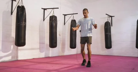 Stepping into boxing ring, male athlete swinging jump rope on padded floor for Stock Footage 344946260