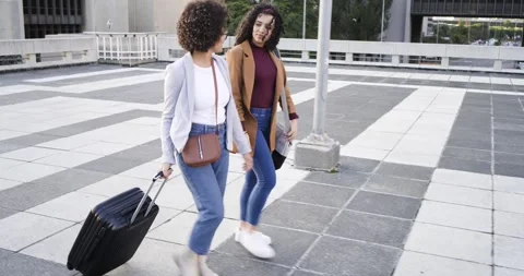 Stepping in, two female friends rolling suitcase, carrying gray bag on rooftop, Stock Footage 339320482