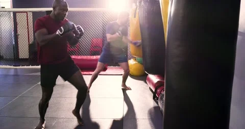 Stepping into view at gym, diverse males throwing bag punches in red and blue Stock Footage 337623909