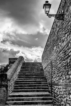 Steps and a stone wall with a mounted light and cloudy sky Stock Photos