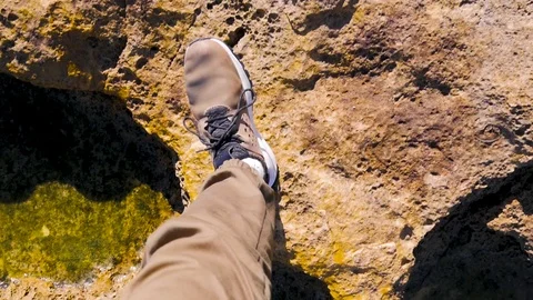 Steps guy in brown sneakers on the rocky surface, green moss, puddles, stones Stock Footage 101813292
