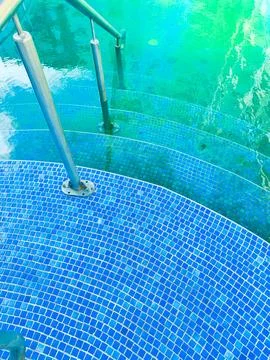 Steps lead into a turquoise pool with bright blue tiles in a sunny location.. 스톡 사진