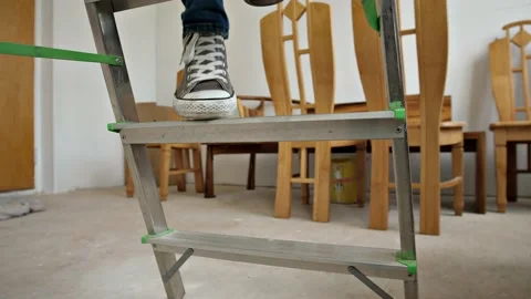 Steps of a stepladder on which a man in sneakers and torn pants is climbing.  Stock Footage 202591912