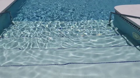 Steps into turquoise sunlit swimming pool.  Light ripples reflection refraction Stock Footage 185553410