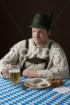 Stereotypical German man in Bavarian costume with a beer and German meal Stock Photos
