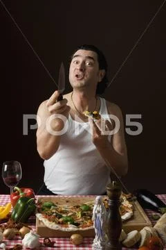 Stereotypical Italian man eating pizza and holding a knife agressively Stock-Fotos