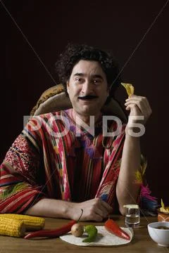 Stereotypical Mexican man with Mexican ingredients eating a tortilla chip Stock Photos