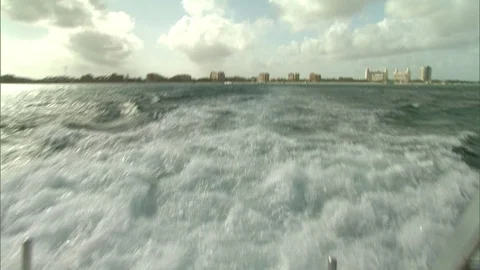 Stern of diving boat with step ladders and wake and buildings on shore line in Video stock 95601318