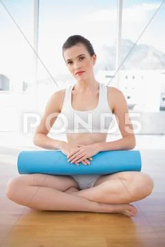 Stern fit brown haired model in sportswear sitting and holding an exercising mat Stock Photos