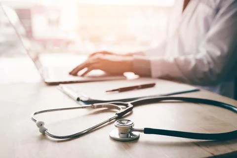 Stethoscope and background doctor using laptop at desk in clinic working on.. Foto stock