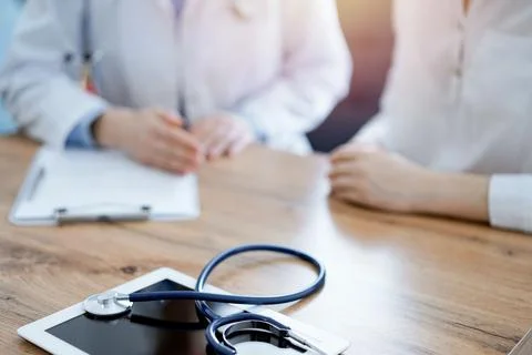 Stethoscope and tablet computer are lying on the wooden table while doctor and Stock Photos