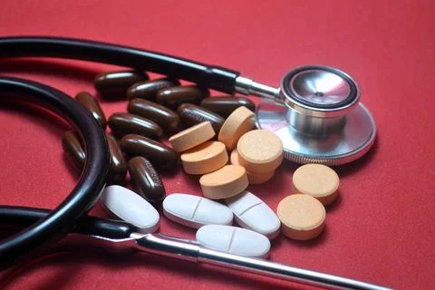 Stethoscope with assorted pills on red surface showcasing essential medical.. Fotos de archivo