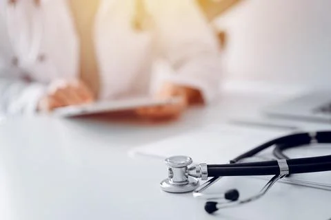 Stethoscope lying at doctor's working desk, close up. Physician uses tablet 库存照片