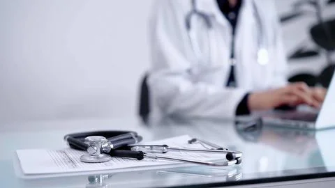 Stethoscope is lying on the glass table while doctor woman is working with Stock Photos