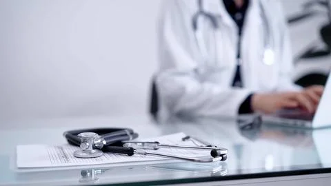 Stethoscope is lying on the glass table while doctor woman is working with Stock Photos