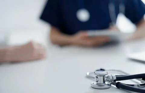 Stethoscope lying on the tablet computer in front of a doctor and patient at the Stockfoto's