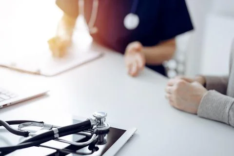 Stethoscope lying on the tablet computer in front of a doctor and patient at the Photos