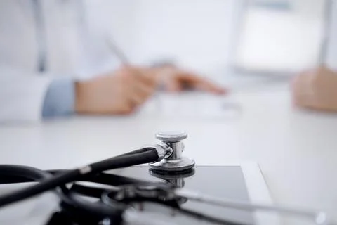 Stethoscope lying on the tablet computer in front of a doctor and patient Stock Photos