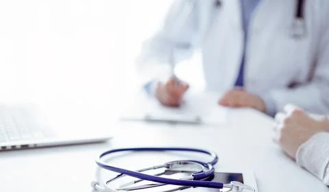 Stethoscope lying on the tablet computer in front of a doctor and patient at the Foto stock