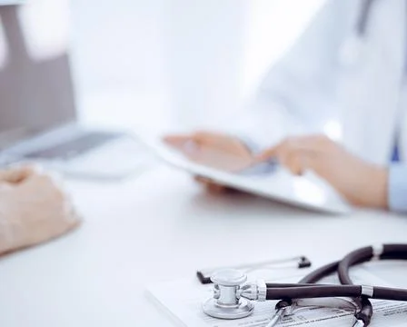 Stethoscope lying on the tablet computer in front of a doctor and patient Photos