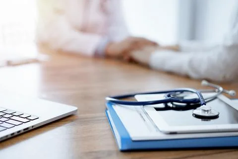 Stethoscope, tablet and laptop computer are lying on the wooden table while Stock Photos