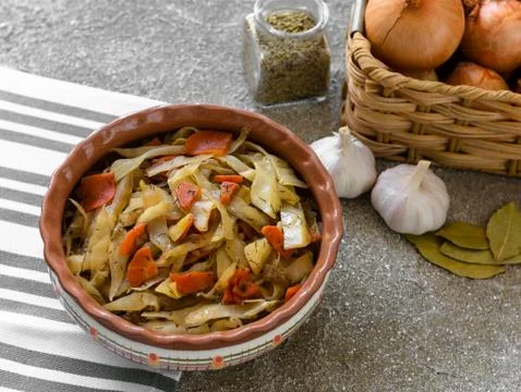 Stewed cabbage in clay bowl with onion garlic and condiments on linen napkin Stock Photos