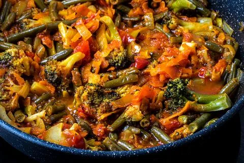 Stewed vegetables in a pan. Cooking process. Vegan food. Stock Photos