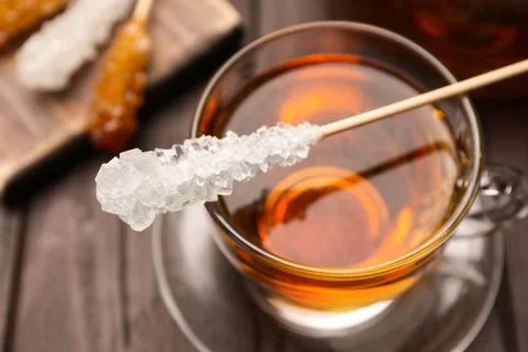 Stick with sugar crystals and cup of tea on wooden table, closeup Stock Photos