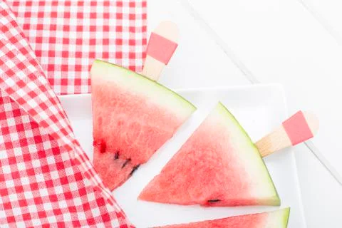 Stick triangular watermelon slice and red plaid picnic cloth. Stock Photos