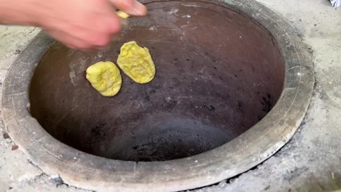 Stick yellow cookie bread dough to the hot circle round clay oven in Stock Footage 250063839