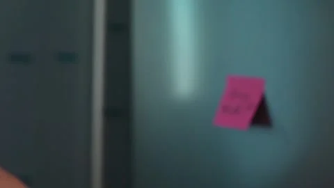 A sticky note with a shopping reminder is attached to a wall in an indoor Vidéo 339096499