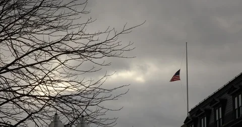 Stiff breeze blows half mast United States flag against stormy grey skies Stock Footage 120859117