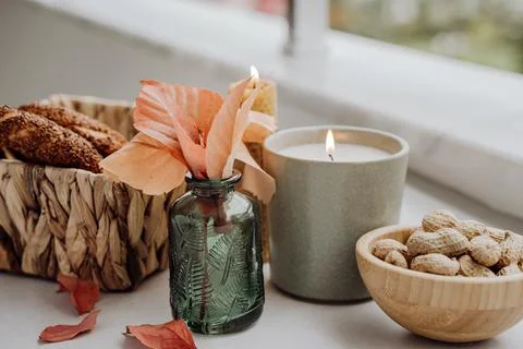 Still life candle flame, peanut, fallen leaves, wicker basket, bagel on a table Stock Photos