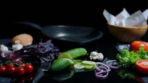 Still life of chef's table on black surface. Pan, knife, fresh vegetables and Stock Footage 92550696