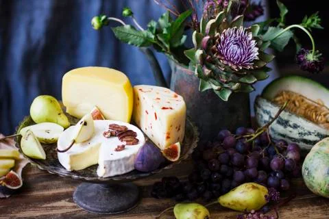 Still life with different cheese, fresh fruit, and garden flowers Stock Photos