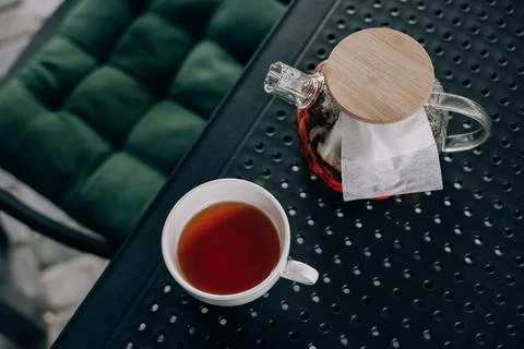 Still life featuring a white cup filled with black tea and a glass teapot Stock Photos
