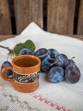 Still life image of an array of plums and a brown clay cup on a picnic table Foto stock