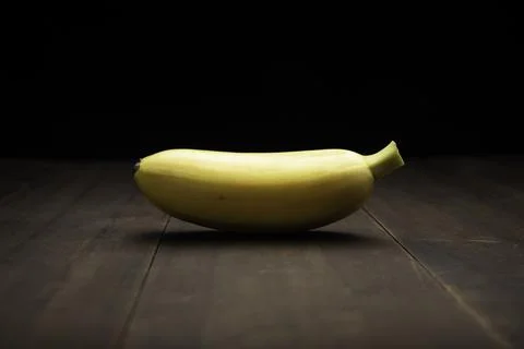 Still life image of one tiny yellow banana close up on rustic wooden surface  Stock Photos