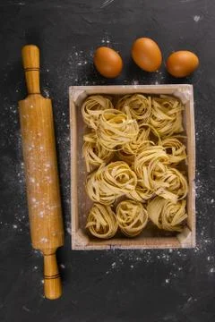 Still life of preparing pasta on rustic wooden background. Raw tagliatelle in Stock Photos