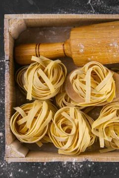 Still life of preparing pasta on rustic wooden background. Raw tagliatelle in Stock Photos