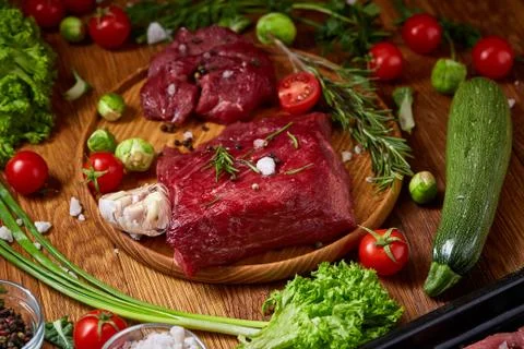 Still life of raw beef meat with vegetables on wooden plate over vintage Stock Photos